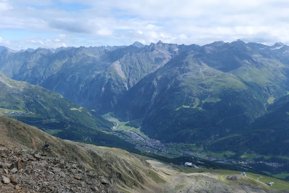A green alpine valley and village far below jagged grey peaks